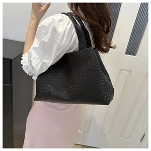 Detalle de bolso tote de cuero trenzado negro llevado al hombro en ambiente casual