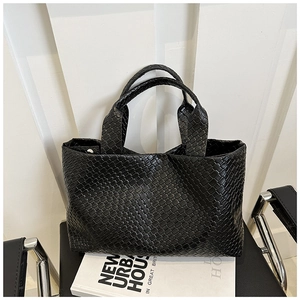 Close-up of black woven leather tote bag with dense diamond texture on a modern chair