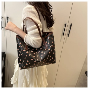 Détail d'un sac cabas noir avec imprimés cerises et anses en cuir marron élégantes