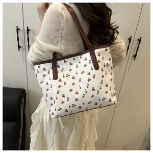 Gros plan du sac cabas blanc à imprimé cerises avec des anses en cuir marron