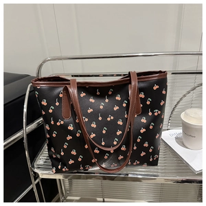Détail du sac cabas noir avec motifs cerises rouges et anses en cuir marron