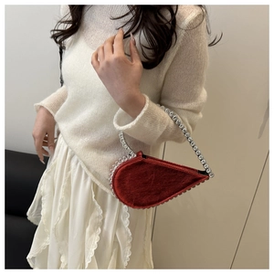 Close-up of heart-shaped red handbag with sparkling rhinestone handle and metallic finish