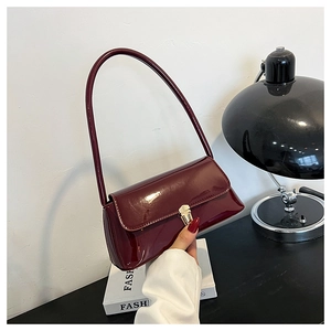 Detail of glossy deep red patent leather underarm bag with gold metal buckle
