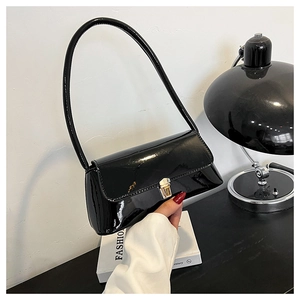 Close-up of glossy black patent leather underarm bag with elegant gold metal buckle closure