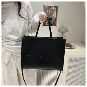 Detail showing the embossed TOTE BAG text on a large black leather crossbody bag