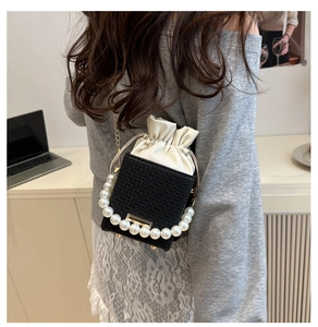Detail of woven black handbag with satin drawstring, pearl handle and gold chain strap