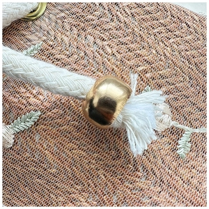 Close-up of straw bag with white lace embroidery detail and golden drawstring metal bead