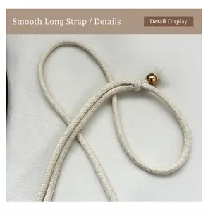 Detail of smooth off-white woven shoulder strap with a decorative golden metal ball charm