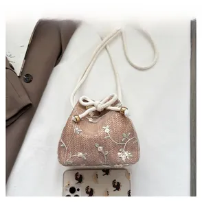 Detail view of woven bucket bag featuring white floral embroidery and cotton rope strap