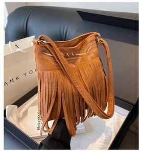 Détail d'un sac seau en daim marron avec franges et broderies dans une boîte cadeau