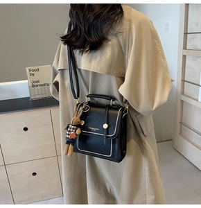 Detalle de bolso bandolera de cuero negro con costuras blancas y colgante de conejo