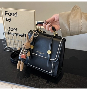Detalle de bolso de cuero negro con costuras blancas y un lindo colgante de conejo