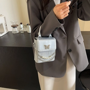 Sac bandoulière argenté avec boucle papillon et chaîne en perles sur veste grise