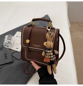 Detalle de bolso de cuero marrón oscuro con borde de perlas y un colgante de conejo