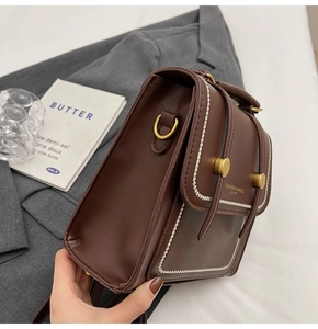 Detalle de bolso bandolera de cuero marrón oscuro con costuras crema y anillos D dorados