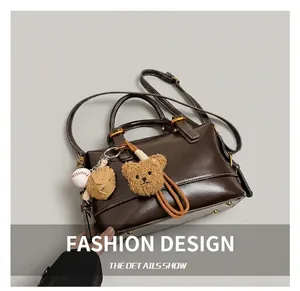 Detail of dark brown faux leather Boston bag with plush bear and baseball pendants