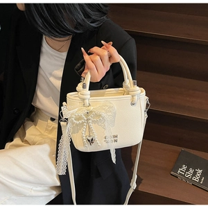 Detail of cream white leather bucket bag with lace bow pendant and silver brand logo