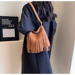 Détail d'un sac seau en daim marron avec de longues franges et une broderie blanche