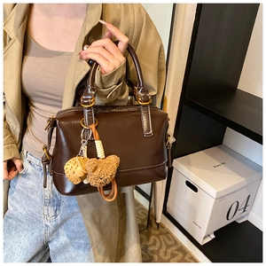 Close-up of vintage brown leather Boston bag with plush bear charm and gold hardware