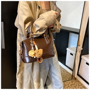 Detail of dark brown Boston bag with plush bear charm and yellow cookie pendant