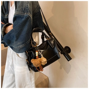 Detail of black Boston bag with white stitching and bear charm on a shoulder strap