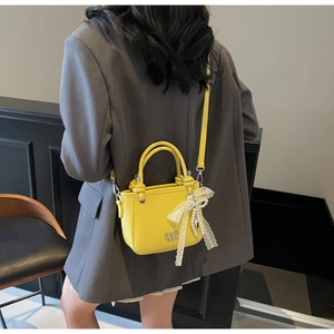Detail van gele emmertas met kanten strik en parel op een grijze oversized blazer