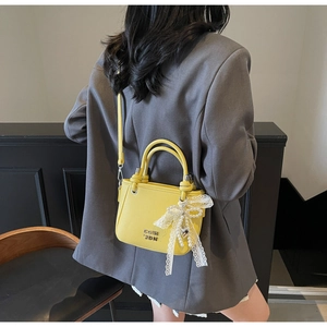 Detail of yellow lychee leather bucket bag with lace bow charm and metallic logo accents