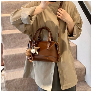 Detail of a brown Boston bag with white stitching and bear charm on a beige trench coat