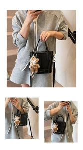Close-up of black glossy bucket bag featuring a plush bear charm and adjustable strap