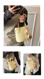 Detail of a light yellow bucket bag with a cute bear plush charm and logo text