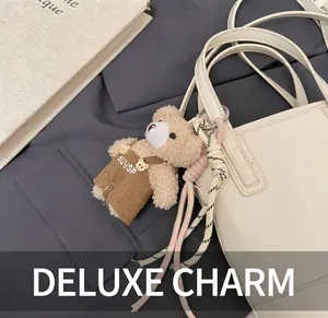 Plush teddy bear charm with corduroy overalls on a white handbag, close-up view