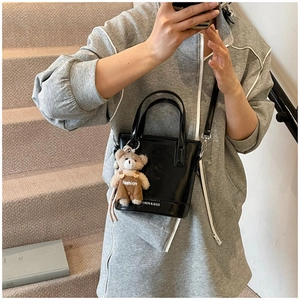 Detail of black glossy bucket bag with teddy bear charm and SHION & BAGS logo on leather