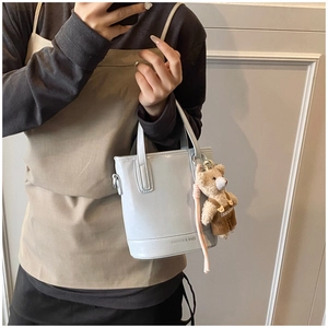 Detail of light blue glossy bucket bag with a cute bear plush charm and text detail