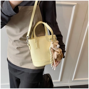 Detailed view of yellow leather bucket bag with bear charm and adjustable shoulder strap