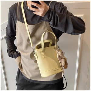 Detail of light yellow bucket bag with plush bear charm and fashion logo print