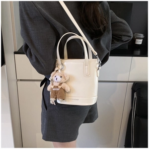 Detail of cream bucket bag with bear pendant and embossed fashion lettering