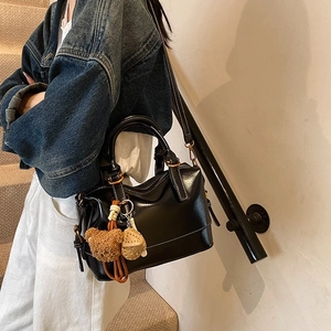 Retro black patent leather Boston bag shown on shoulder with teddy bear charm