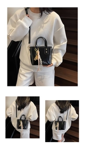 Detail of glossy black patent leather bucket bag with metal key and woven charms