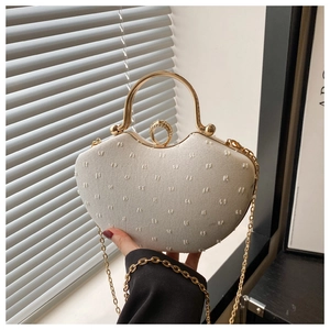 Close-up of cream heart evening bag with rhinestone ring clasp and golden handle