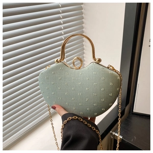 Detail of light green heart-shaped bag with gold circular handle and diamond clasp