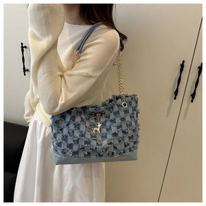 Detail of blue checkerboard denim tote bag featuring frayed edges and gold deer pendant