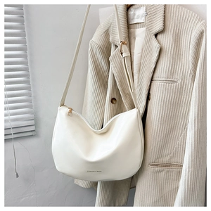 Dettaglio borsa hobo beige minimalista con cerniera dorata appesa a un blazer