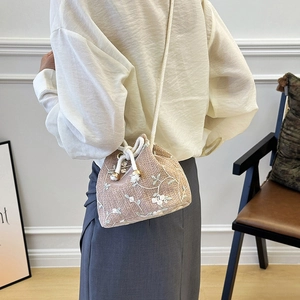 Straw woven bucket bag with white floral embroidery and drawstring strap on model