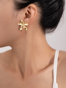 Macro detail of gold layered flower earrings worn by a model for a festive party look