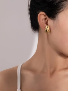 Detail of gold liquid metal flower earrings featuring a textured wavy surface on model