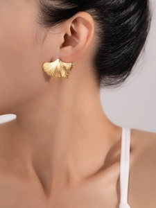 Macro detail of golden ginkgo leaf earrings with radial texture on a female model