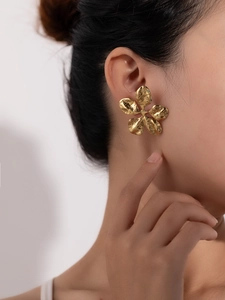 Detail of oversized gold flower stud earring with hammered metal texture on model