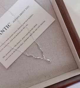 Macro detail of curved S925 silver necklace with fluid wave links and teardrop pendant