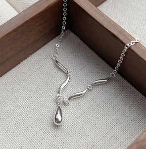 Macro shot of polished silver water drop pendant and curved S925 sterling silver chain
