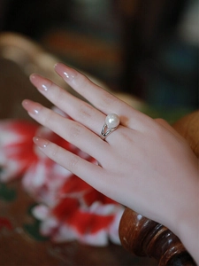 Detail shot of an elegant pearl ring on a hand with a vintage red floral background